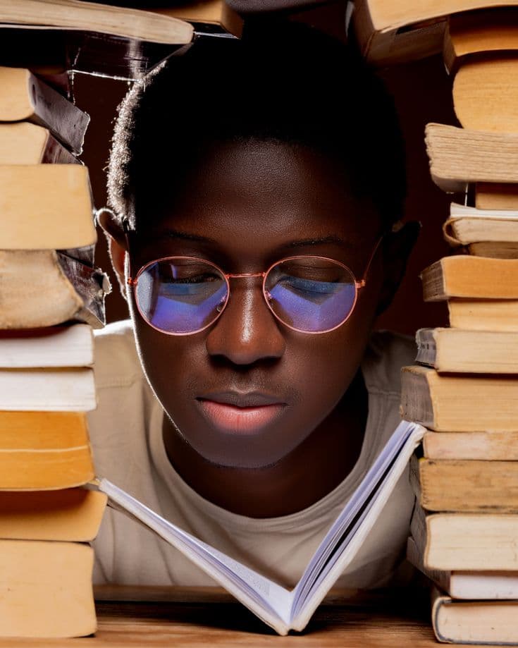 Student reading a book surrounded by stacks of books